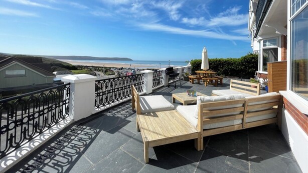 Een balkon met een houten bankje en een tafel, met uitzicht op een strand en de oceaan.