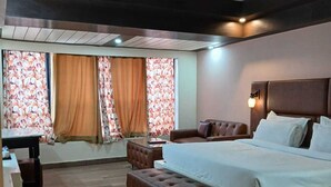 A hotel room with a large bed, a sofa, a desk, and a window with curtains. - Hotel Drive Inn Mussoorie (Mussoorie)