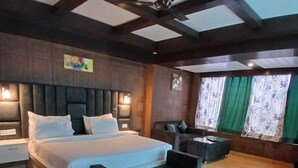 A spacious bedroom with a large bed, a sofa, a desk, and a ceiling fan. - Hotel Drive Inn Mussoorie (Mussoorie)