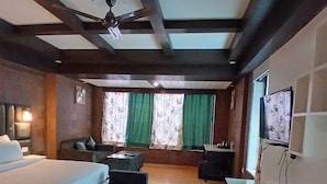 A hotel room with a large bed, a sofa, a TV, and a ceiling fan. - Hotel Drive Inn Mussoorie (Mussoorie)