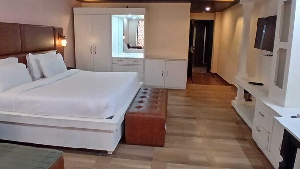 A modern hotel room with a large bed, a seating area, a TV, and a mirror. - Hotel Drive Inn Mussoorie (Mussoorie)