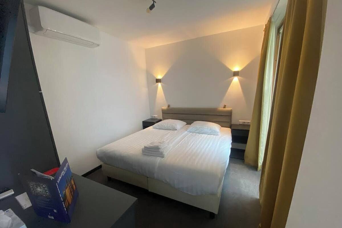 A hotel room with a bed, bedside tables, and a desk with a book and papers.