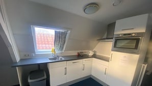 A compact kitchen with white cabinets, a built-in oven, and a window with curtains. - Hotel La Noire - Delft City Centre (Delft)