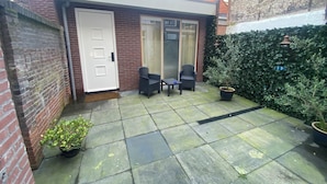 A small patio area with a white door, two chairs, a table, and a potted plant. - Hotel La Noire - Delft City Centre (Delft)