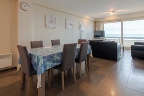 A dining area with a table set for six, a sofa, and a TV in a room with a large window overlooking the sea. - Family Spot by the Coastal Trails (Middelkerke)