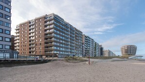 A high-rise hotel with multiple floors, a beach in the foreground, and a distinctive circular building in the background. - Family Spot by the Coastal Trails (Middelkerke)