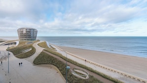 A modern architectural structure with a circular design, adjacent to a beach with a walkway and grassy areas. - Family Spot by the Coastal Trails (Middelkerke)