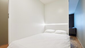 A modern hotel room with a large bed, a wooden floor, and a dark-colored wall unit.