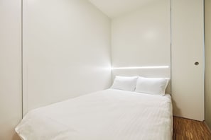 A minimalist bedroom with a bed, white walls, and a wooden floor. - Résidence du Lys Apartments (Luxembourg City)