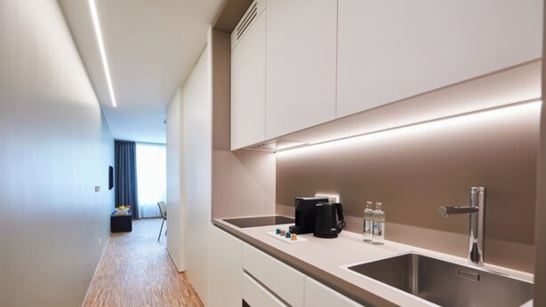 A modern kitchen with white cabinets, stainless steel appliances, and a long countertop.