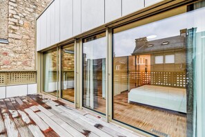 Habitación de hotel moderna con grandes puertas correderas de vidrio, una terraza de madera y vistas a un edificio tradicional.