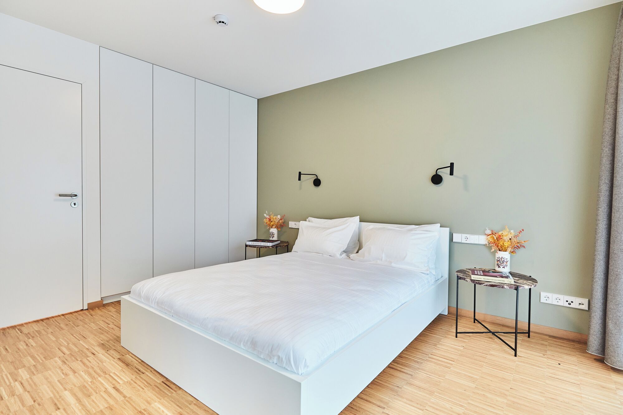 Une chambre moderne avec un grand lit, une armoire, une table de chevet avec une lampe et une petite table sur laquelle est posé un vase.