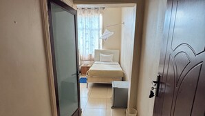 Un pasillo estrecho que conduce a un dormitorio con una cama, una mesita de noche y una pequeña mesa.