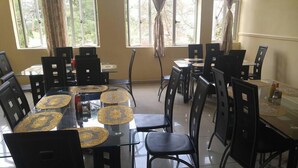 Un comedor con varias mesas y sillas, ventanas amplias con cortinas y piso de baldosas.