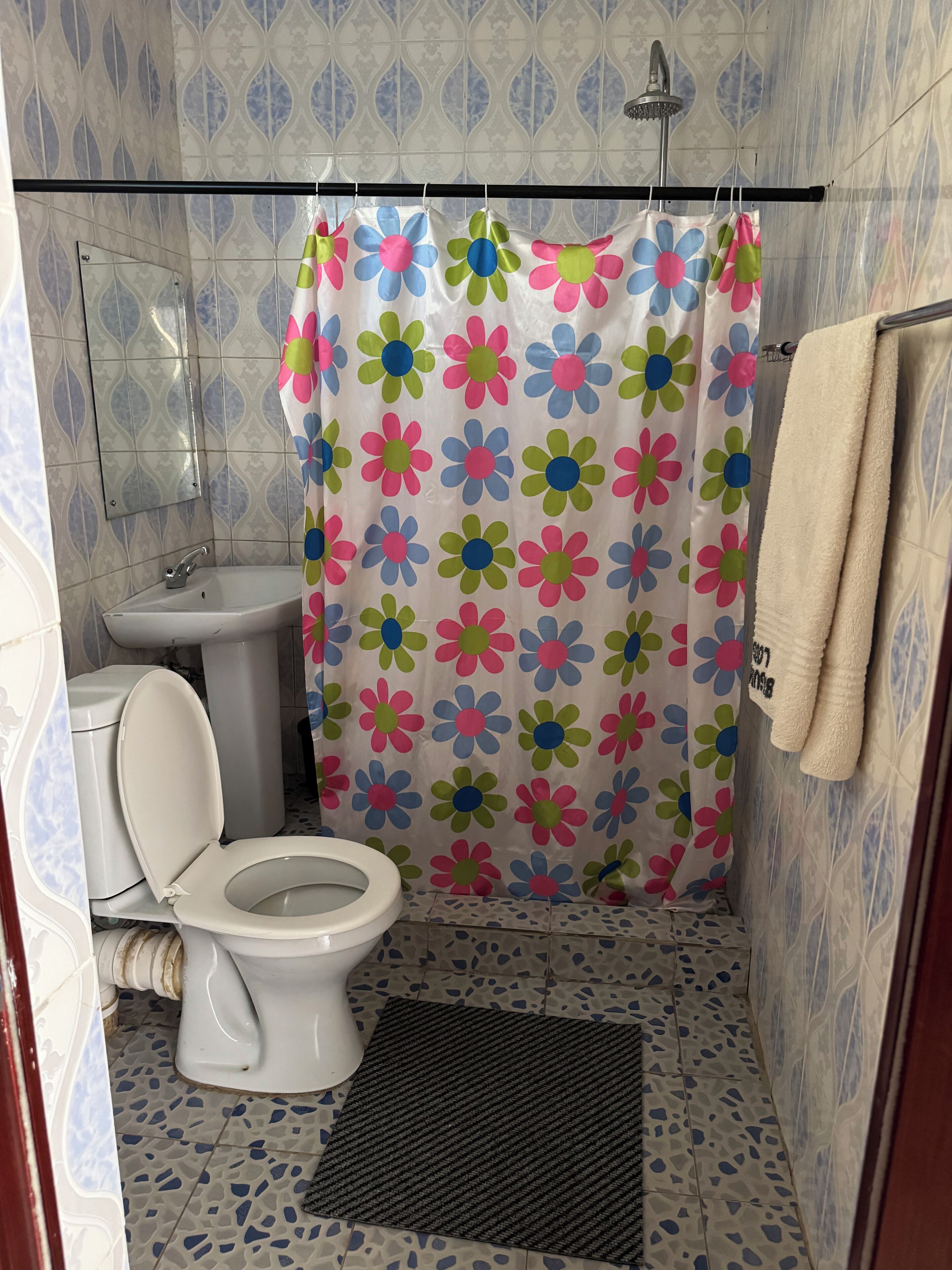 Un baño con inodoro, lavamanos, ducha y cortina de ducha con estampado floral.
