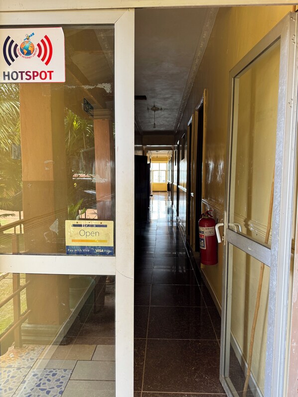 Un pasillo de hotel con un extintor, un letrero que indica pago con Visa y una puerta de vidrio con el logotipo de HOTSPOT.