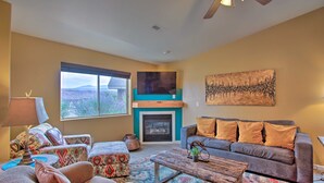 A living room with a fireplace, a sofa, a coffee table, and a large window with a view. - 3444 Views, Garage and backyard, Shared Pool and Hot Tub! (Moab)