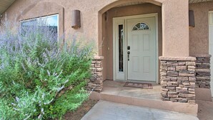A house with a stone facade, a white door with a glass panel, and a small porch area. - 3444 Views, Garage and backyard, Shared Pool and Hot Tub! (Moab)