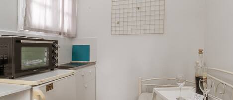A compact kitchenette with a microwave, a small sink, and a window with curtains.
