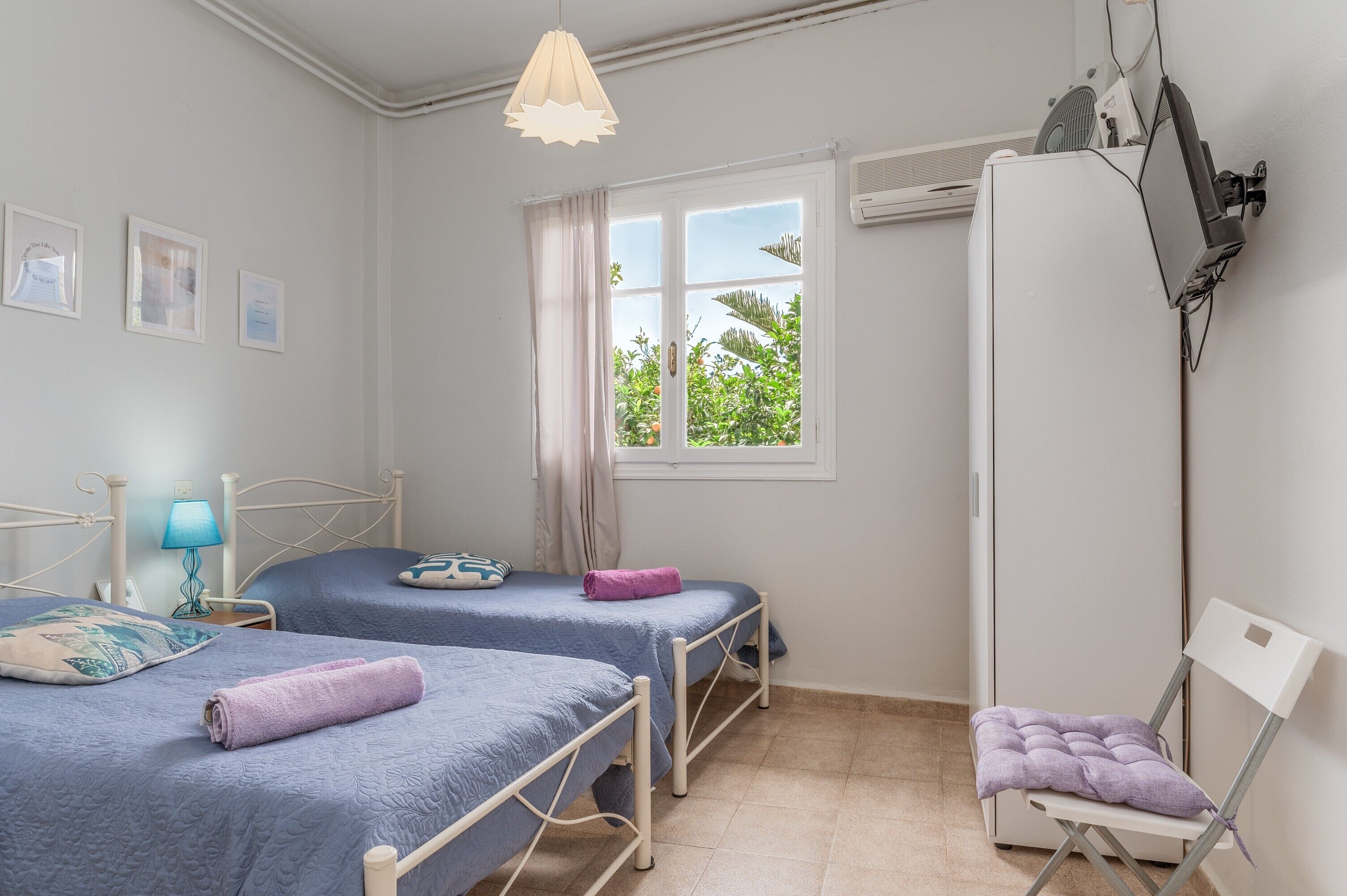 A bedroom with two beds, a chair, a desk, a window with curtains, and a wall-mounted air conditioner.