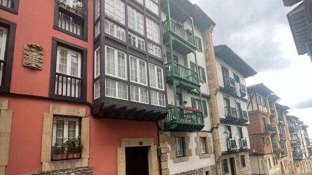 A street with buildings featuring traditional architecture, including balconies and windows with shutters.
