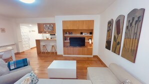 A modern living room with a sofa, a coffee table, and a kitchen area with wooden cabinets and a TV.