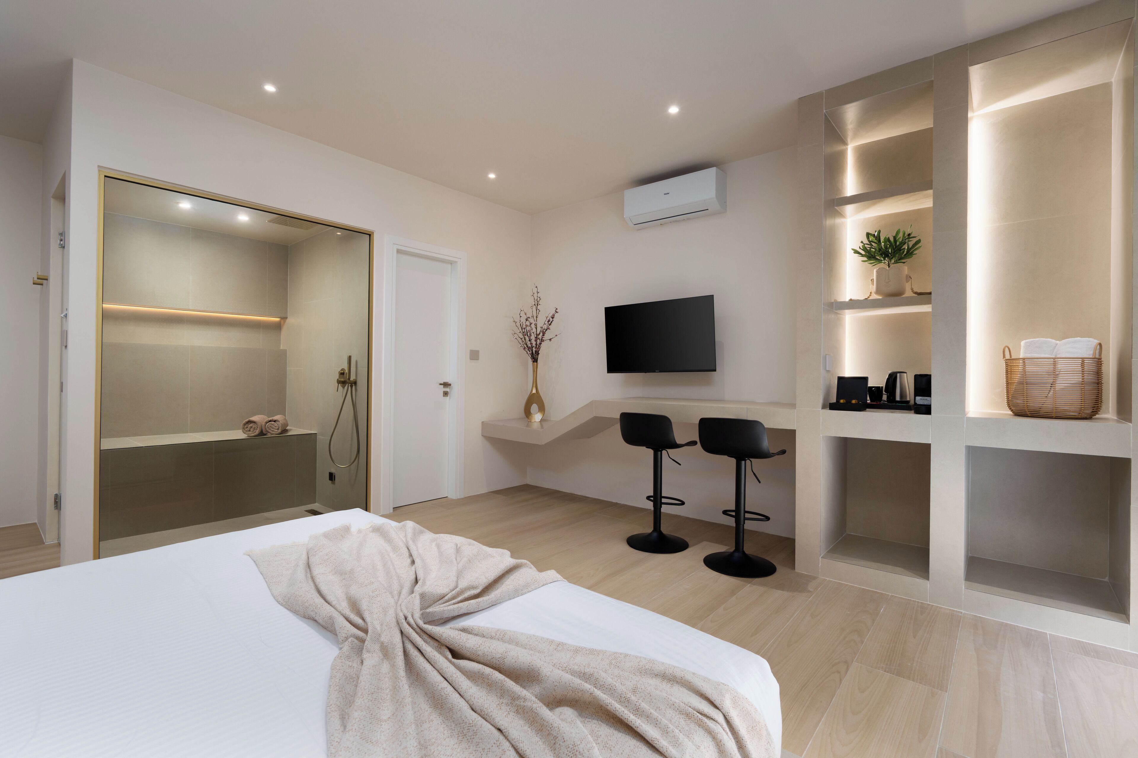 Una habitación de hotel moderna con una cama grande, un vestidor, un televisor y un área de descanso con dos sillones.