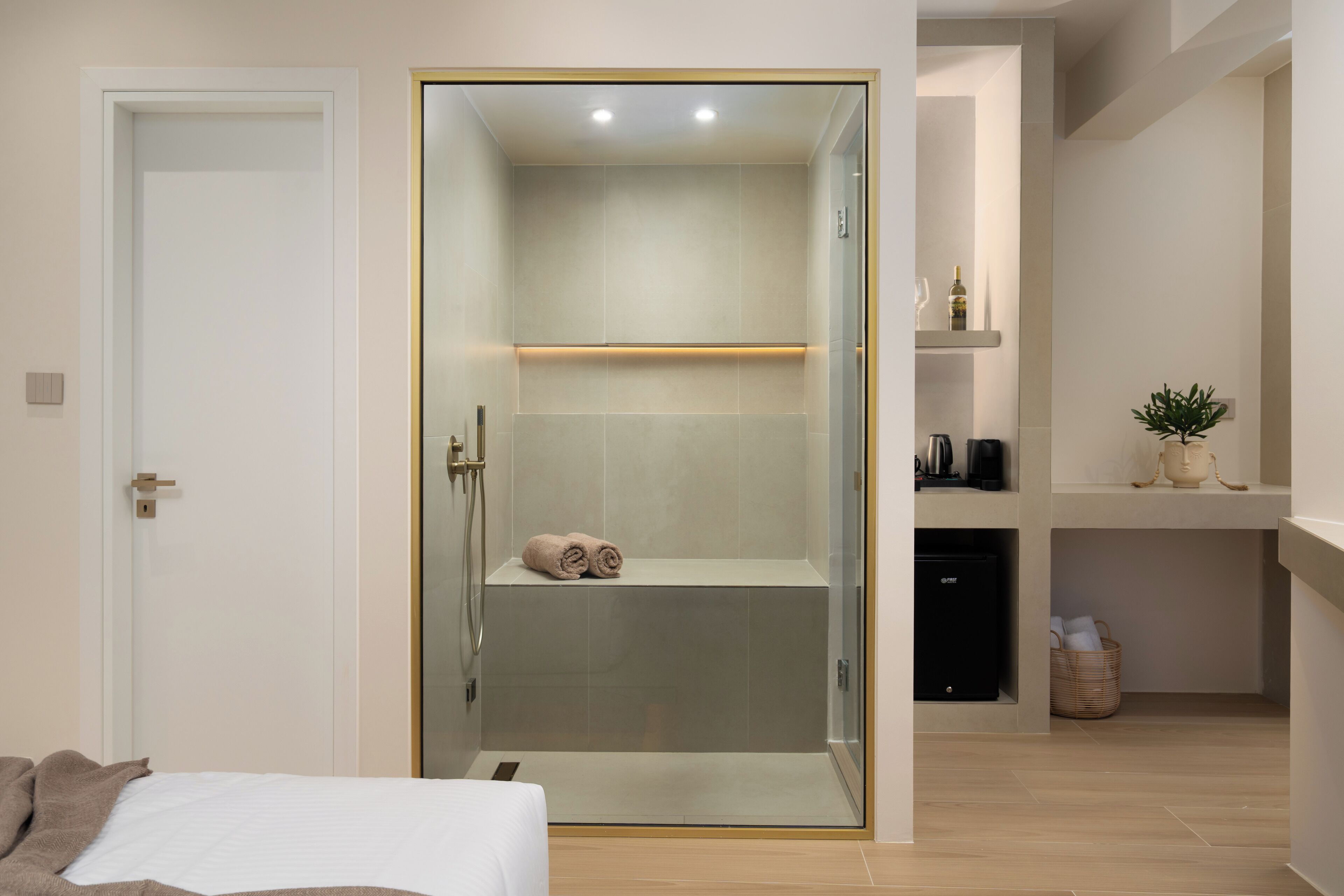 A modern bathroom with a glass-enclosed shower, a towel on the floor, and a small shelf with toiletries.