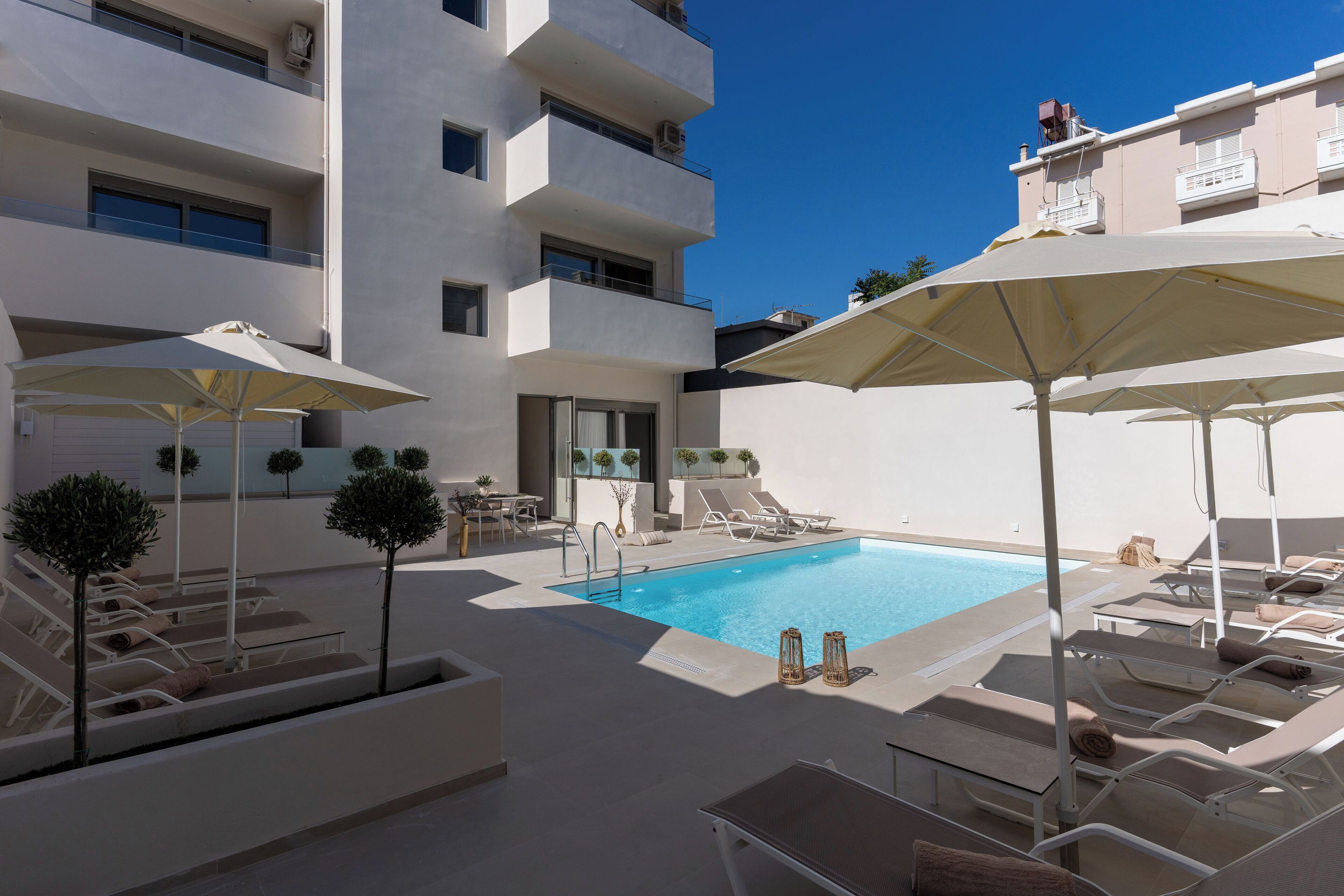 A pool area with sun loungers and umbrellas, surrounded by a white building with multiple balconies.