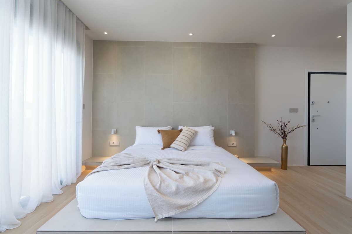 A modern bedroom with a large bed, bedside lamps, and a vase with branches.