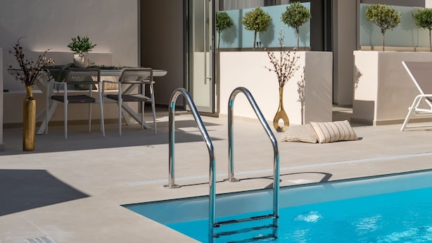 A modern pool area with a clear blue pool, a metal ladder, and a dining area with a table and chairs. - Selected Suites  (Chania)