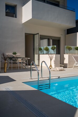 A modern pool area with a clear blue pool, a metal ladder, and a dining area with a table and chairs. - Selected Suites  (Chania)