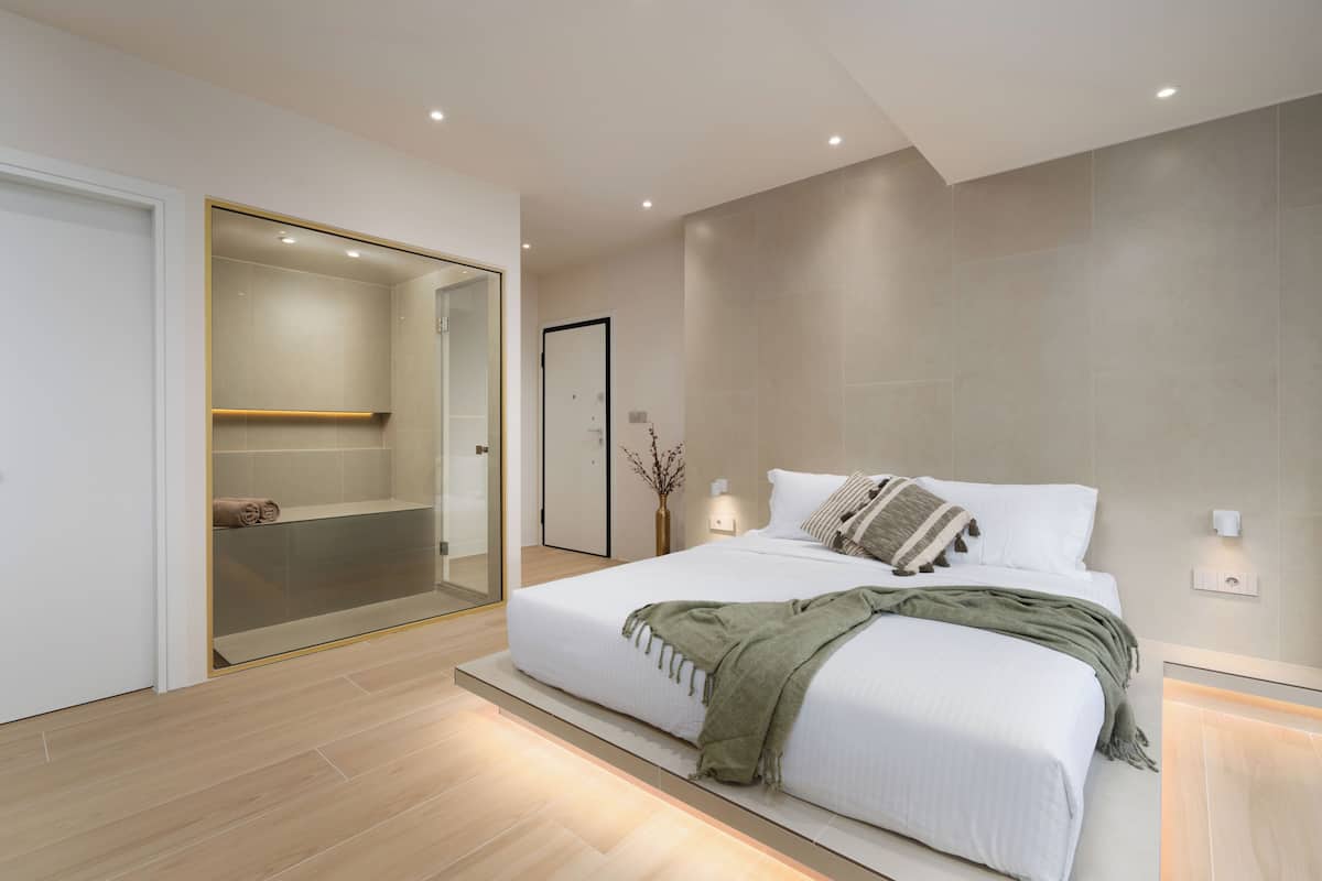A modern bedroom with a large bed, a walk-in closet, and a glass shower enclosure.