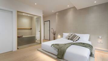 A modern bedroom with a large bed, a walk-in closet, and a glass shower enclosure.