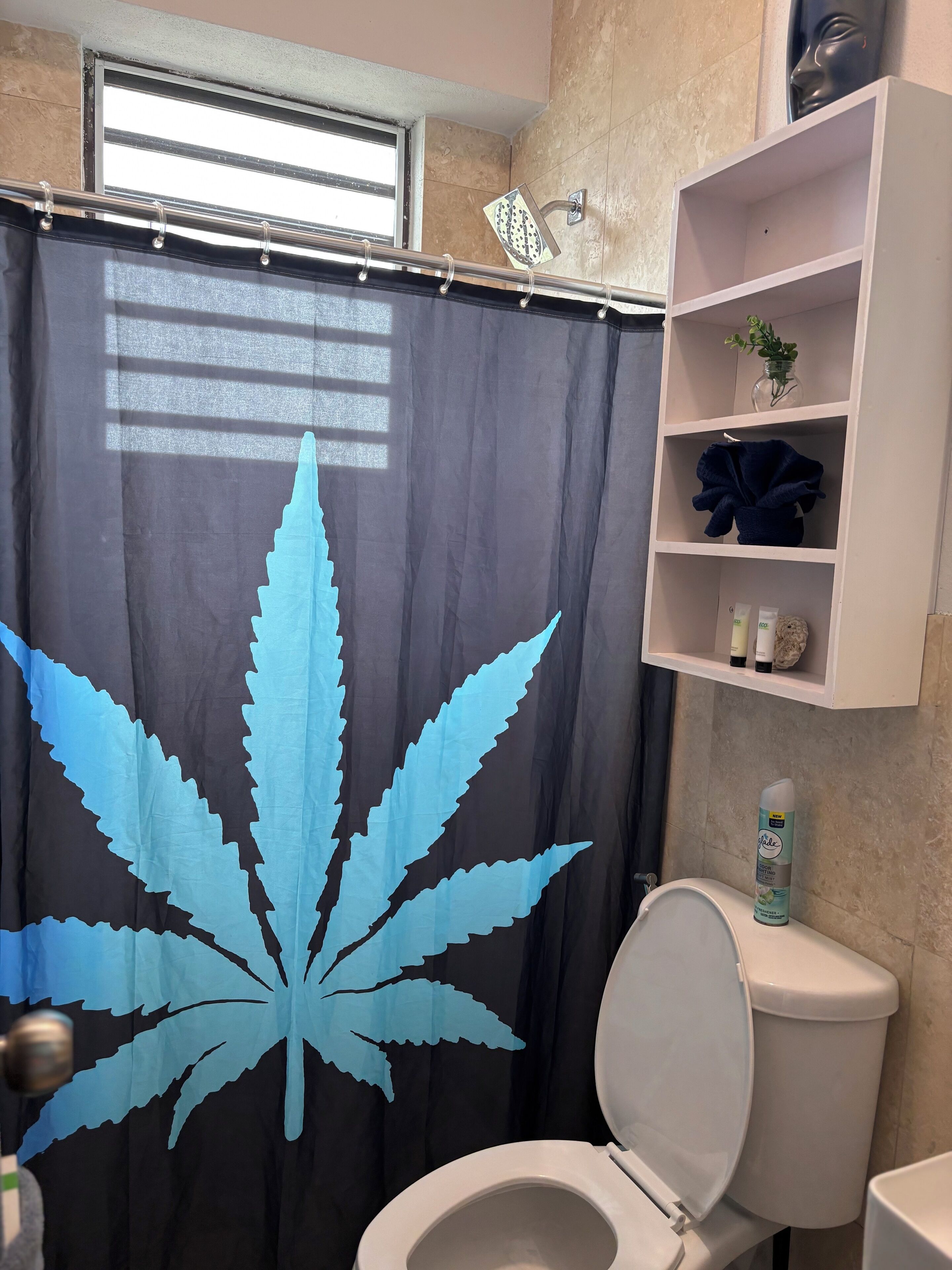 Une salle de bain avec des toilettes, une étagère contenant des articles de toilette et un rideau de douche orné de motifs de feuilles.