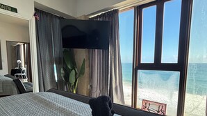 A hotel room with a bed, a TV, a desk, and a large window overlooking the beach. - BednBong Experience Stay (Arecibo)