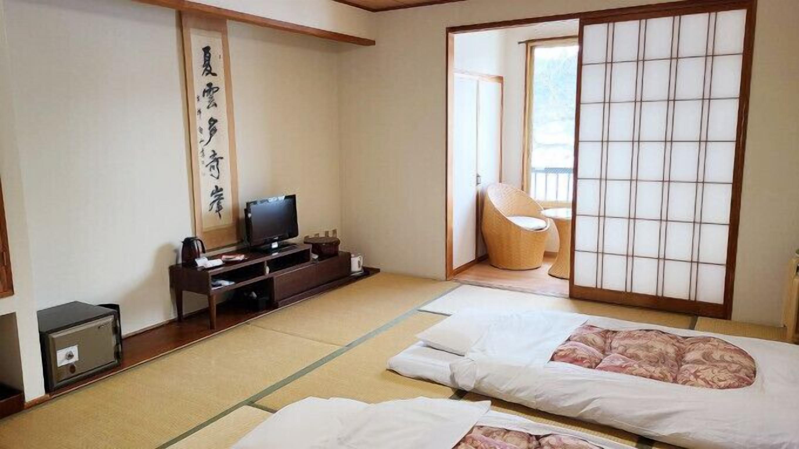 Une pièce de style japonais traditionnel, avec un sol recouvert de tatamis, une télévision, un bureau et une porte coulissante donnant sur un balcon.