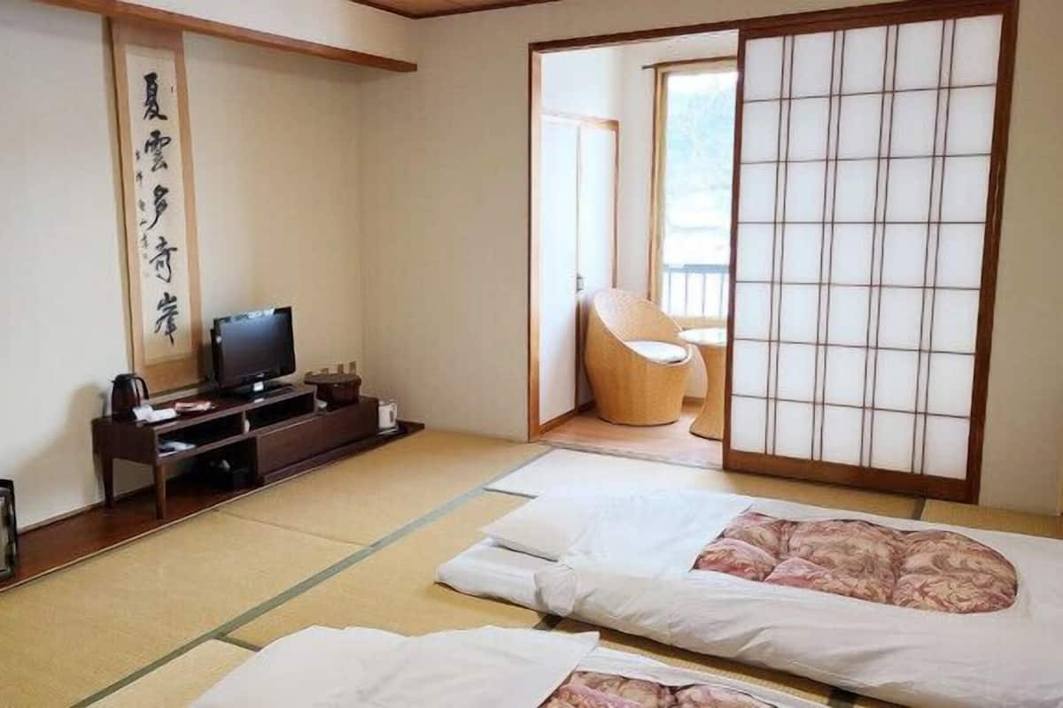 Une pièce de style japonais traditionnel, avec un sol recouvert de tatamis, une télévision, un bureau et une porte coulissante donnant sur un balcon.