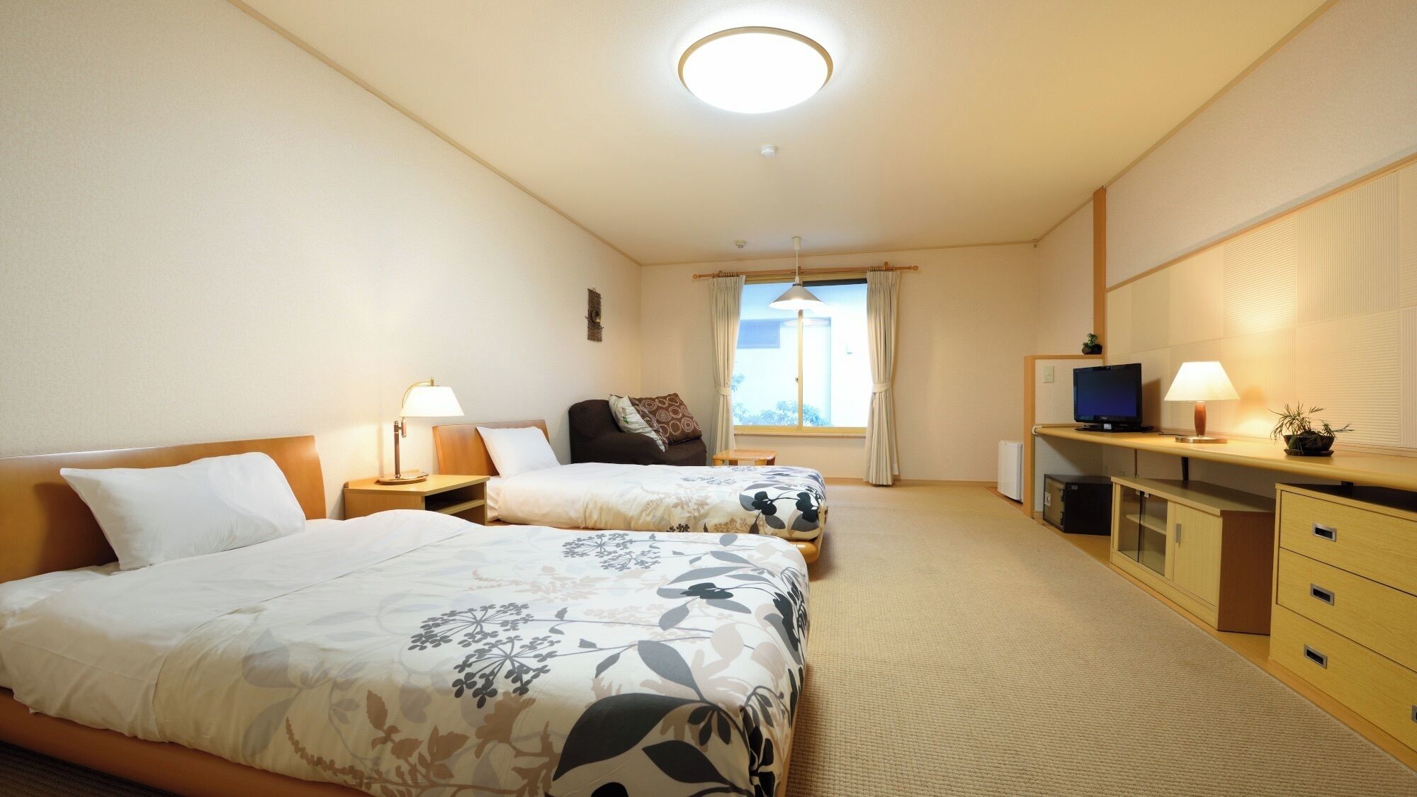 Une chambre d’hôtel avec deux lits, une télévision, un bureau et une fenêtre.