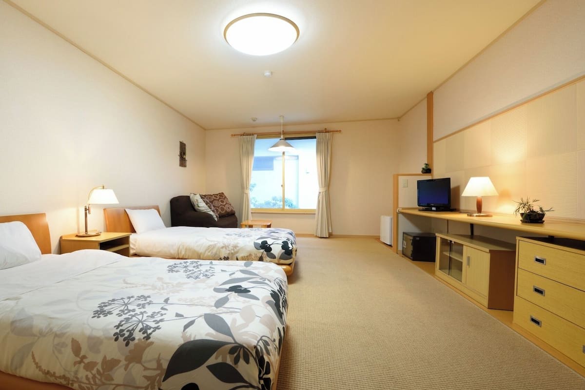Une chambre d’hôtel avec deux lits, une télévision, un bureau et une fenêtre.