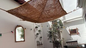 Une terrasse avec une table en bois, des bancs et un auvent suspendu. On y trouve également des plantes en pot et un barbecue.