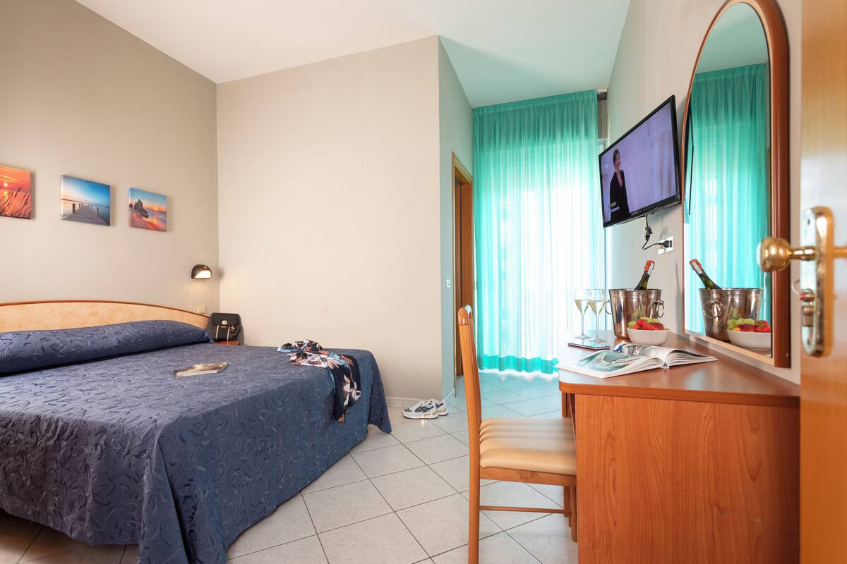 Habitación de hotel con dos camas, un escritorio de madera con espejo, televisión y ventana con cortinas.