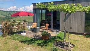 A modern building with a patio area featuring outdoor furniture and a red umbrella. - MoselHoch vacation cottage in the vineyards of Klüsserath (Klüsserath)