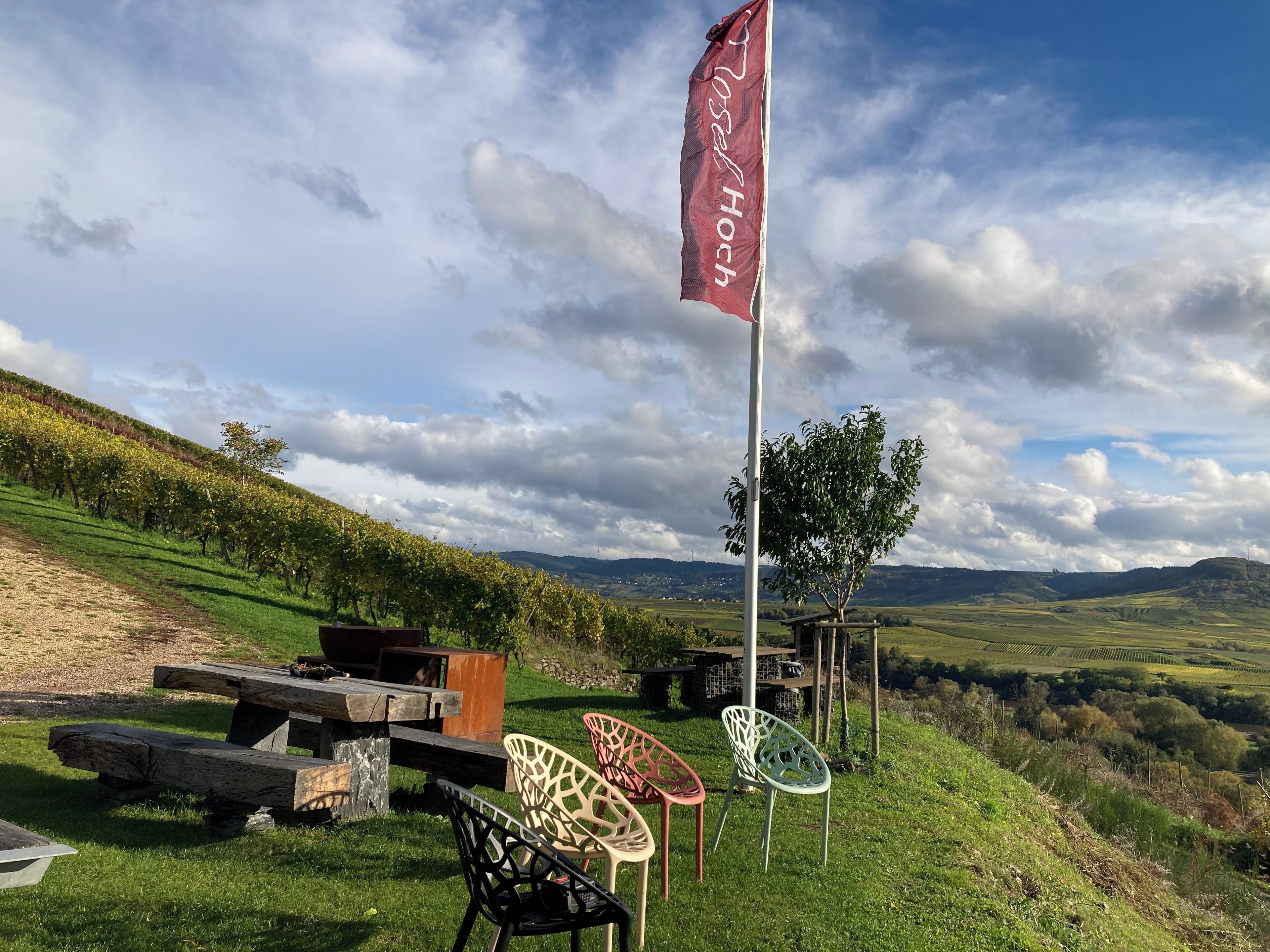 Een picknickplaats met een vlag, picknicktafel en stoelen, met een mooi heuvellandschap op de achtergrond.