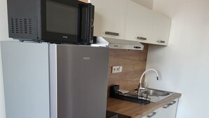 Cocina compacta con refrigerador de acero inoxidable, microondas, encimera de madera, lavamanos y armarios blancos.