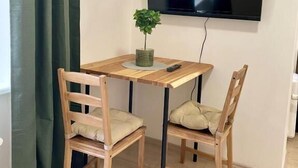 Una habitación pequeña con una mesa de madera y dos sillas, un televisor montado en la pared y una cortina verde.