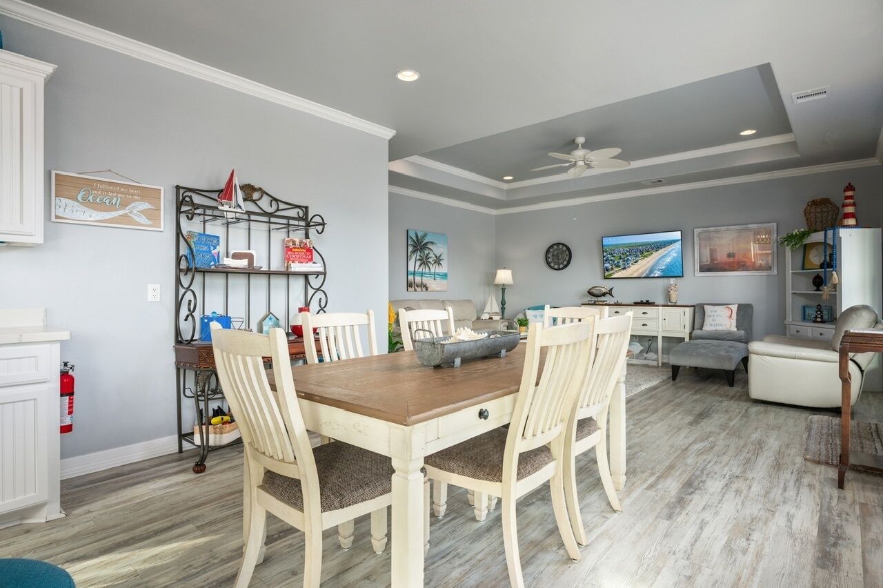 A dining area with a wooden table and white chairs, a bookshelf, and a television in the background.