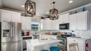 A modern kitchen with white cabinetry, stainless steel appliances, and a central island with stools. - Big Chill 2 Bedroom Home (Port Bolivar)