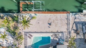 An aerial view of a resort with a swimming pool, sun loungers, and a sandy beach area.