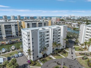 A multi-story hotel with a central courtyard, surrounded by other buildings, a marina, and a view of the ocean. - Casa Marina 432 Newly Remodeled, Water View 2 Bedroom Condo (Fort Myers Beach)